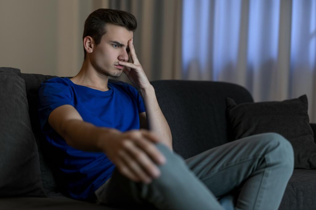 ai prompt: young man looking tired and demotivated after staying up late, sitting on a sofa, low energy, realistic photo