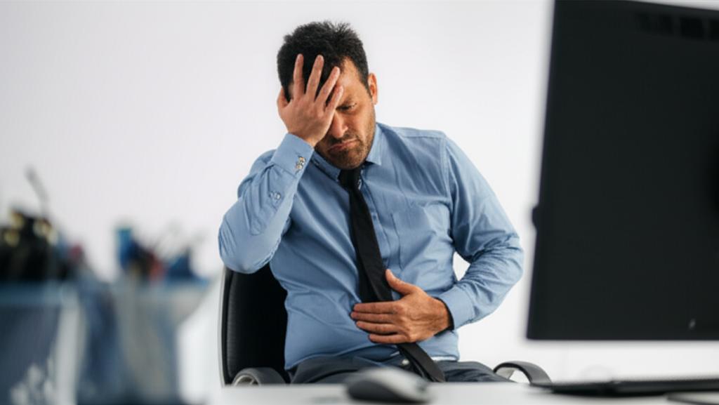 Office worker feeling discomfort from incomplete urination, sitting at desk with stressed expression